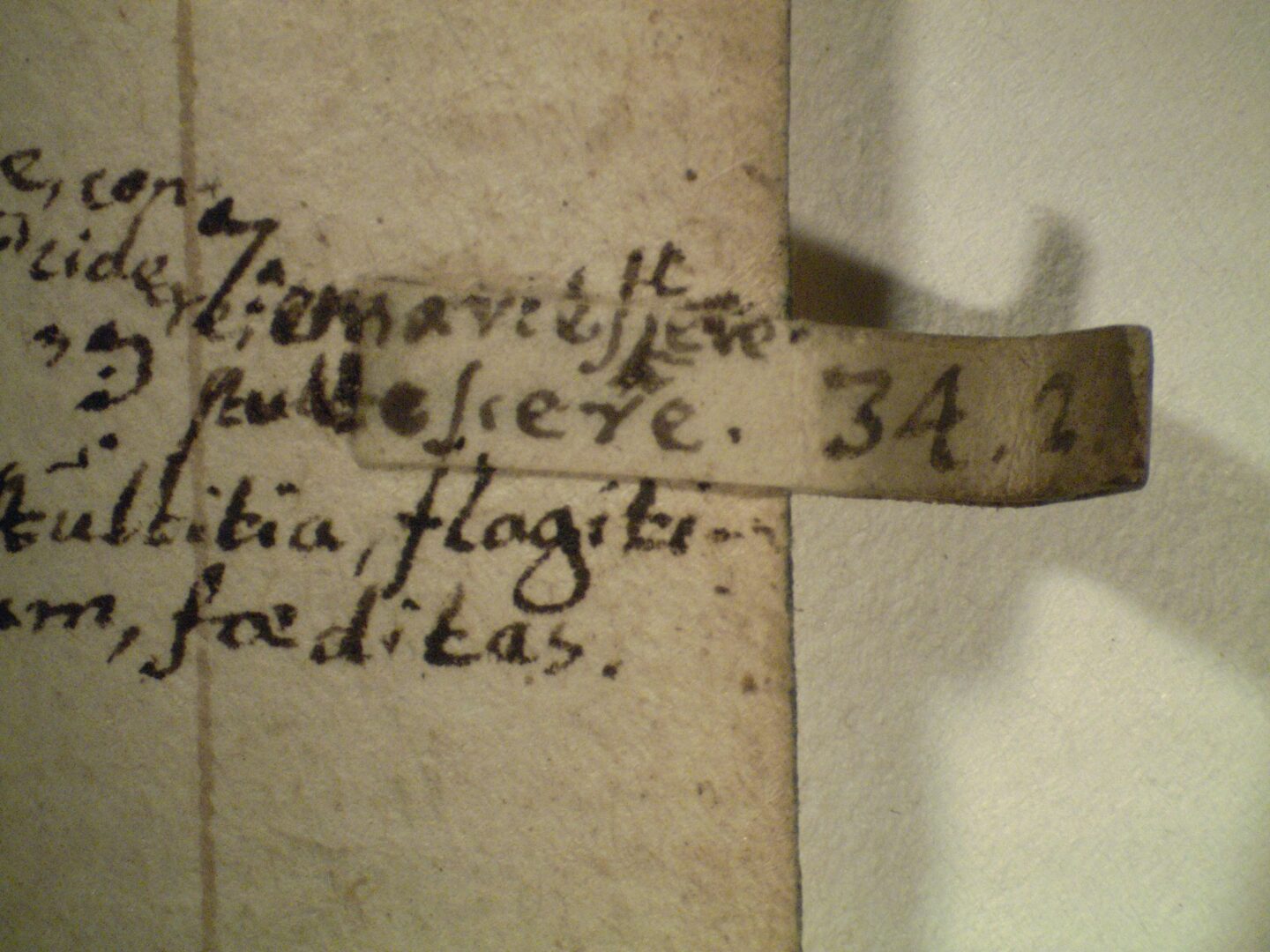 Part of an old page with a small parchment tab pasted to the fore-edge, on which chapter and verse (34.2) are written in a small, neat hand