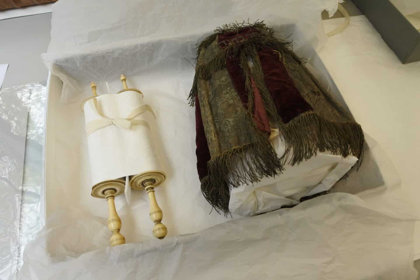 The parchment scroll, partially open, and its red and gold covering mantle are lying side-by-side, in protective tissue